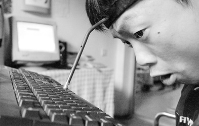 刘洪正在用箍在头上的“脑门按键器”敲击电脑键盘输入文字