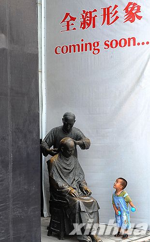 在王府井步行街上，一位儿童在饶有兴趣地观看一座再现老北京民俗的铜雕（7月2日摄）