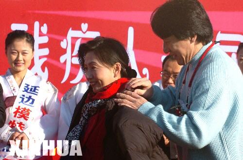 11月16日,成龙为一残疾人穿上羽绒服。